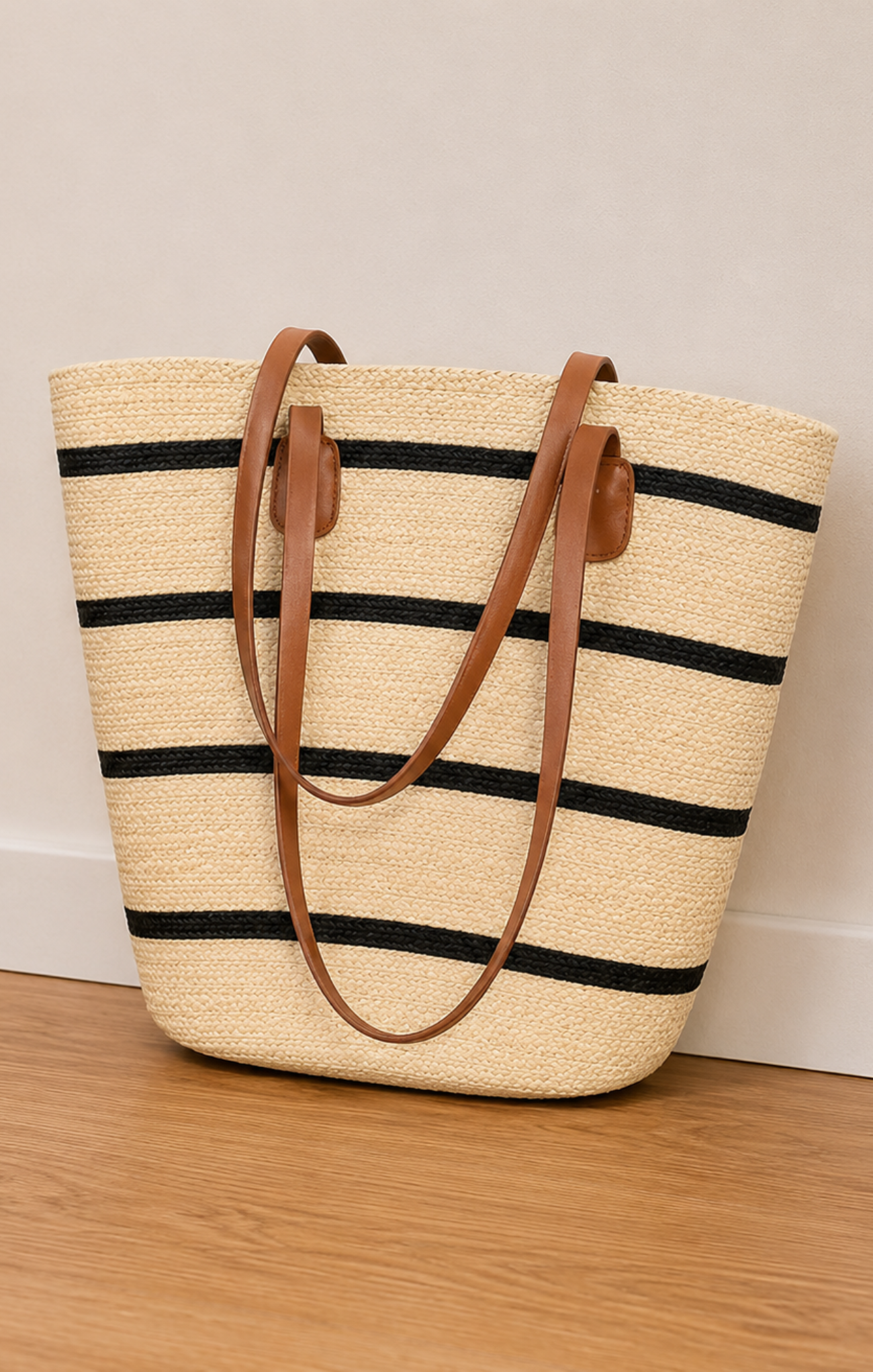 Straw tote bag with black stripes and brown handles on a wooden floor.