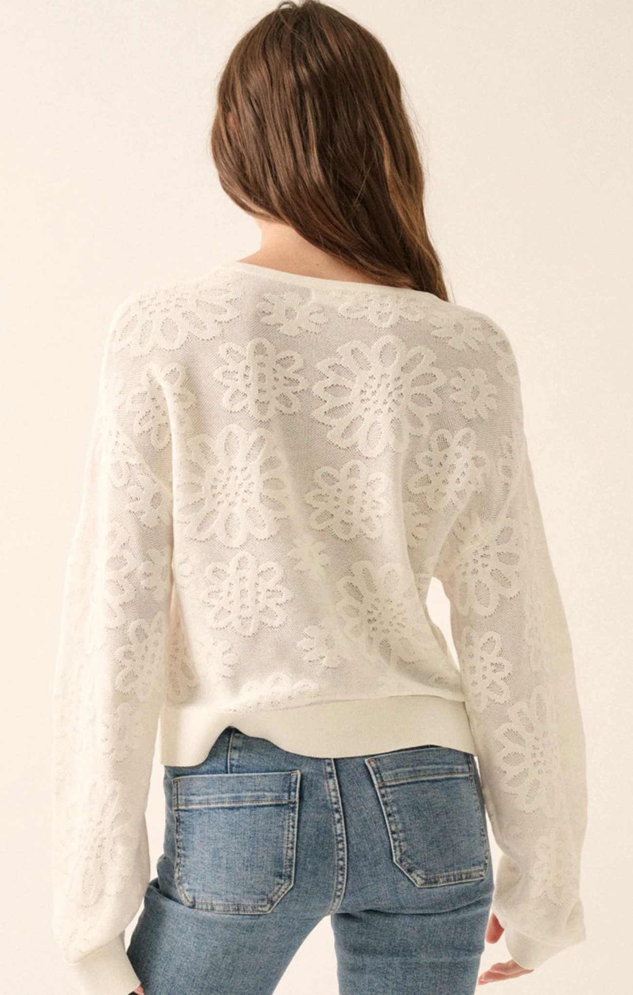 Person wearing a white lace top and blue jeans on a plain background