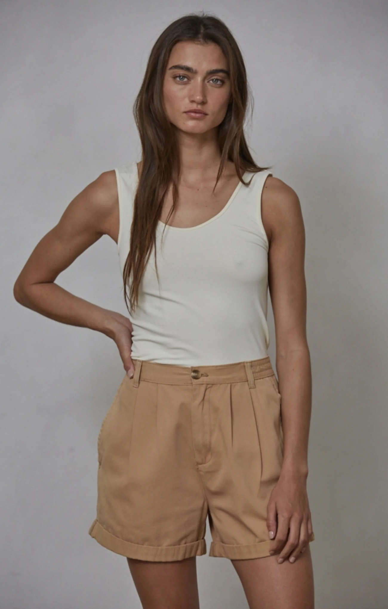 Woman wearing a white tank top and beige shorts against a plain background