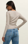 Woman wearing a beige long-sleeve top and blue jeans on a plain background