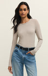 Woman wearing a beige long-sleeve top and blue jeans on a plain background