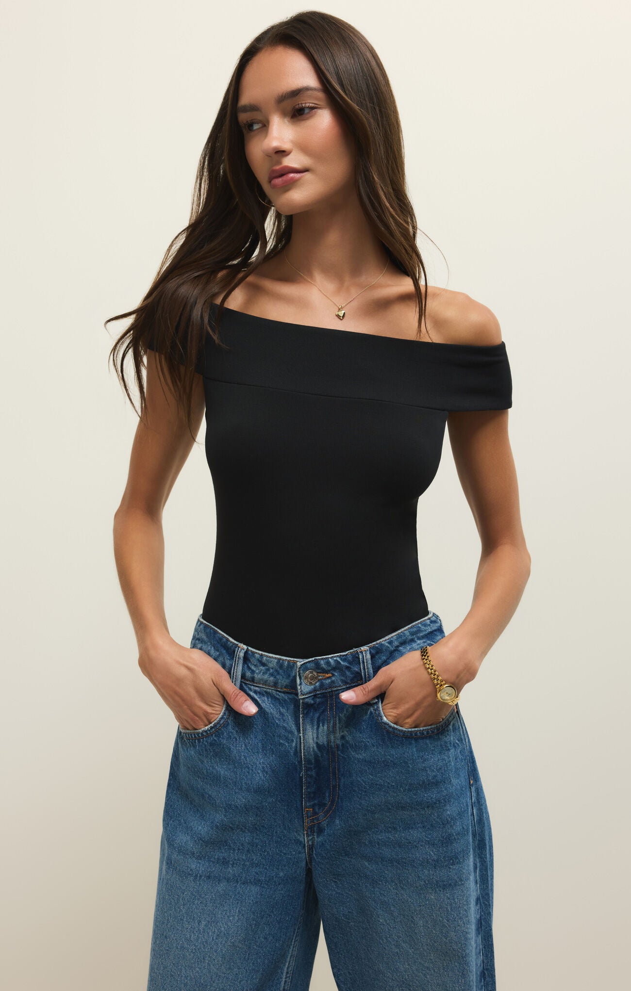 Woman wearing a black off-shoulder top and blue jeans against a plain background
