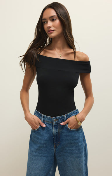 Woman wearing a black off-shoulder top and blue jeans against a plain background