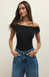 Woman wearing a black off-shoulder top and blue jeans against a plain background