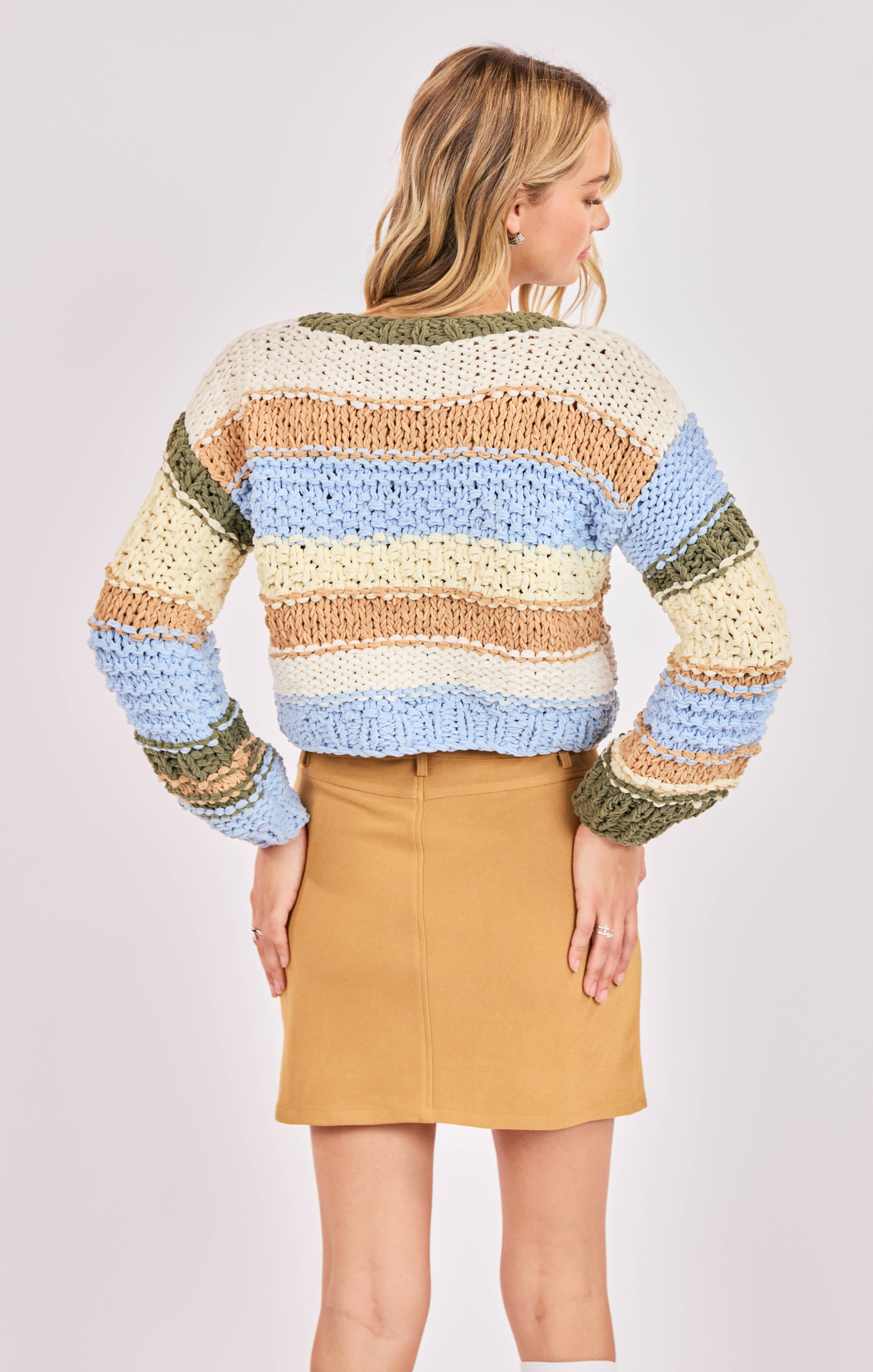 Woman wearing a colorful striped sweater and beige skirt on a white background