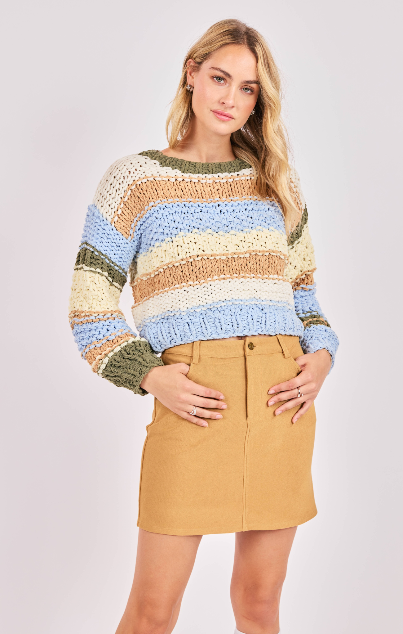 Woman wearing a colorful striped sweater and beige skirt on a white background