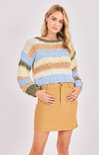 Woman wearing a colorful striped sweater and beige skirt on a white background