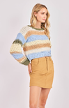 Woman wearing a colorful striped sweater and tan skirt on a white background