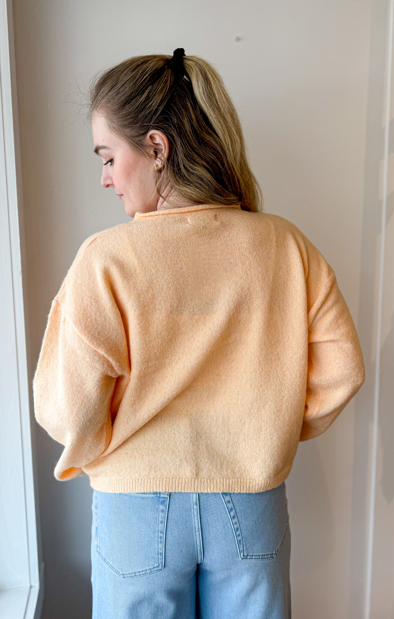 Person wearing a light orange sweater and blue jeans against a plain background