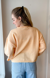 Person wearing a light orange sweater and blue jeans against a plain background