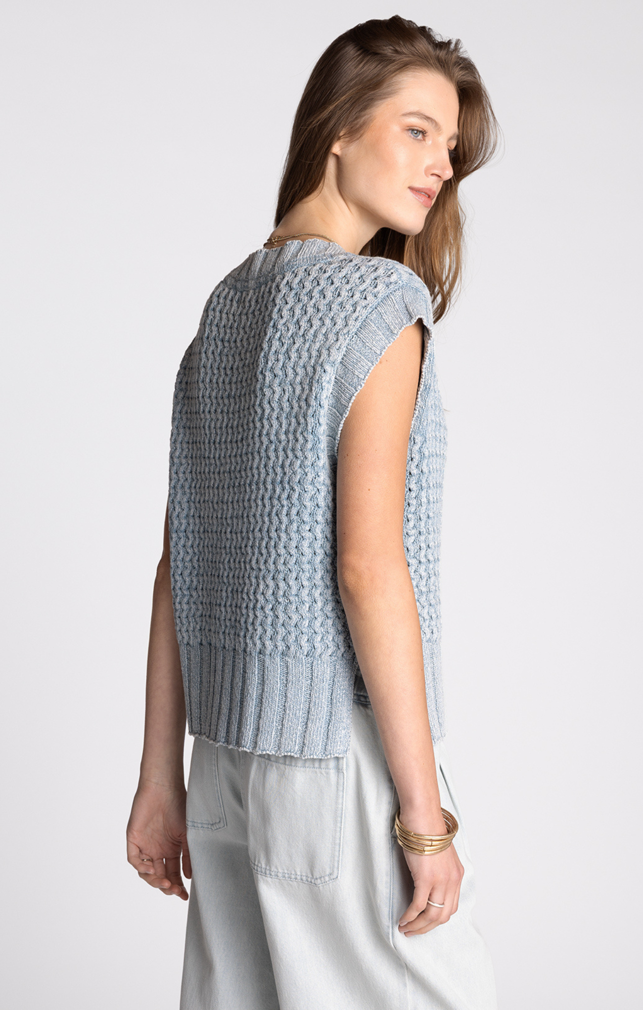 Woman wearing a light blue knitted vest against a white background