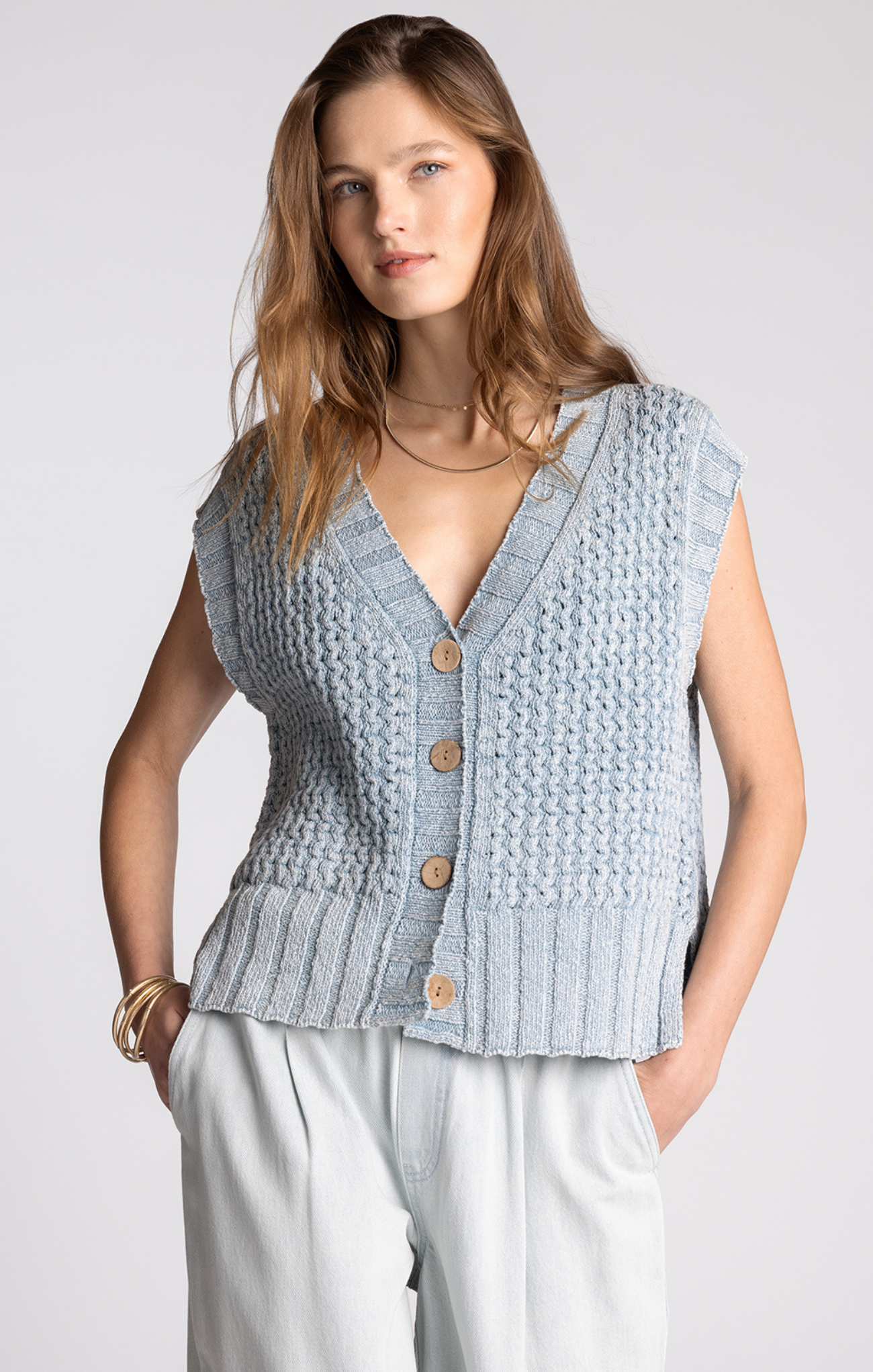Woman wearing a light blue knitted vest with buttons on a white background
