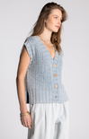 Woman wearing a light blue knitted vest with buttons on a white background