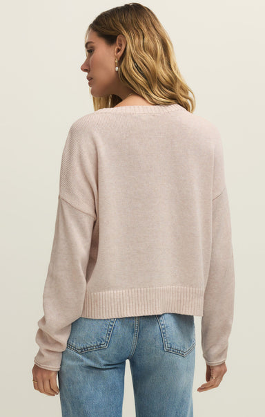 Woman wearing a beige sweater and blue jeans on a plain background