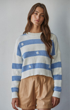 Woman wearing a blue and white striped sweater with beige shorts against a plain background