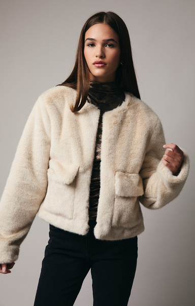 Woman wearing a cream fur jacket against a plain background