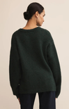 Person wearing a dark green sweater against a beige background