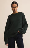 Woman wearing a dark green sweater and dark pants against a beige background