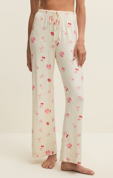 White pajama pants with pink floral patterns worn by a person on a beige background