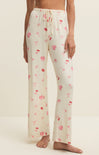 White pajama pants with pink floral patterns worn by a person on a beige background