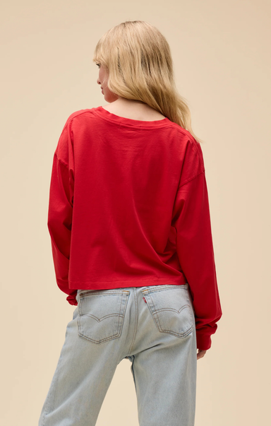 Person wearing a red sweatshirt and light blue jeans on a beige background