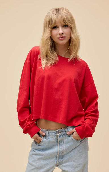 Person wearing a red cropped sweatshirt and light blue jeans against a beige background