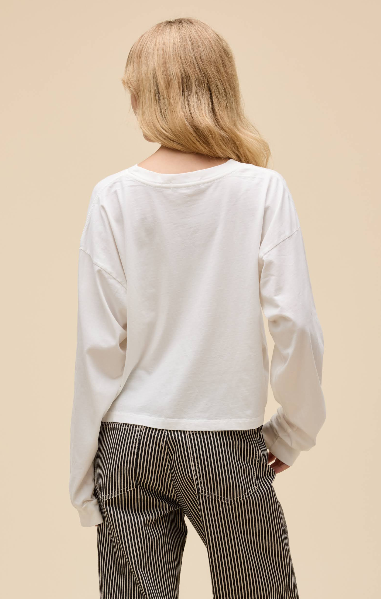 Person wearing a white long-sleeve top and striped pants on a beige background