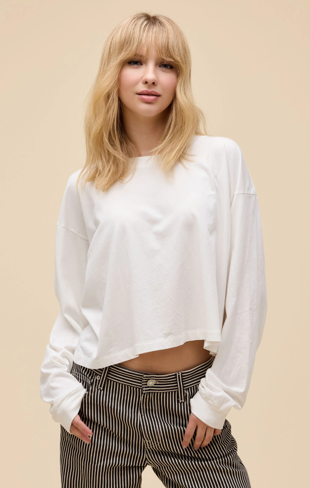 Woman wearing a white long-sleeve top and striped pants on a beige background