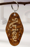 Keychain with 'Aries' engraving on a wooden tag, hanging from a branch.