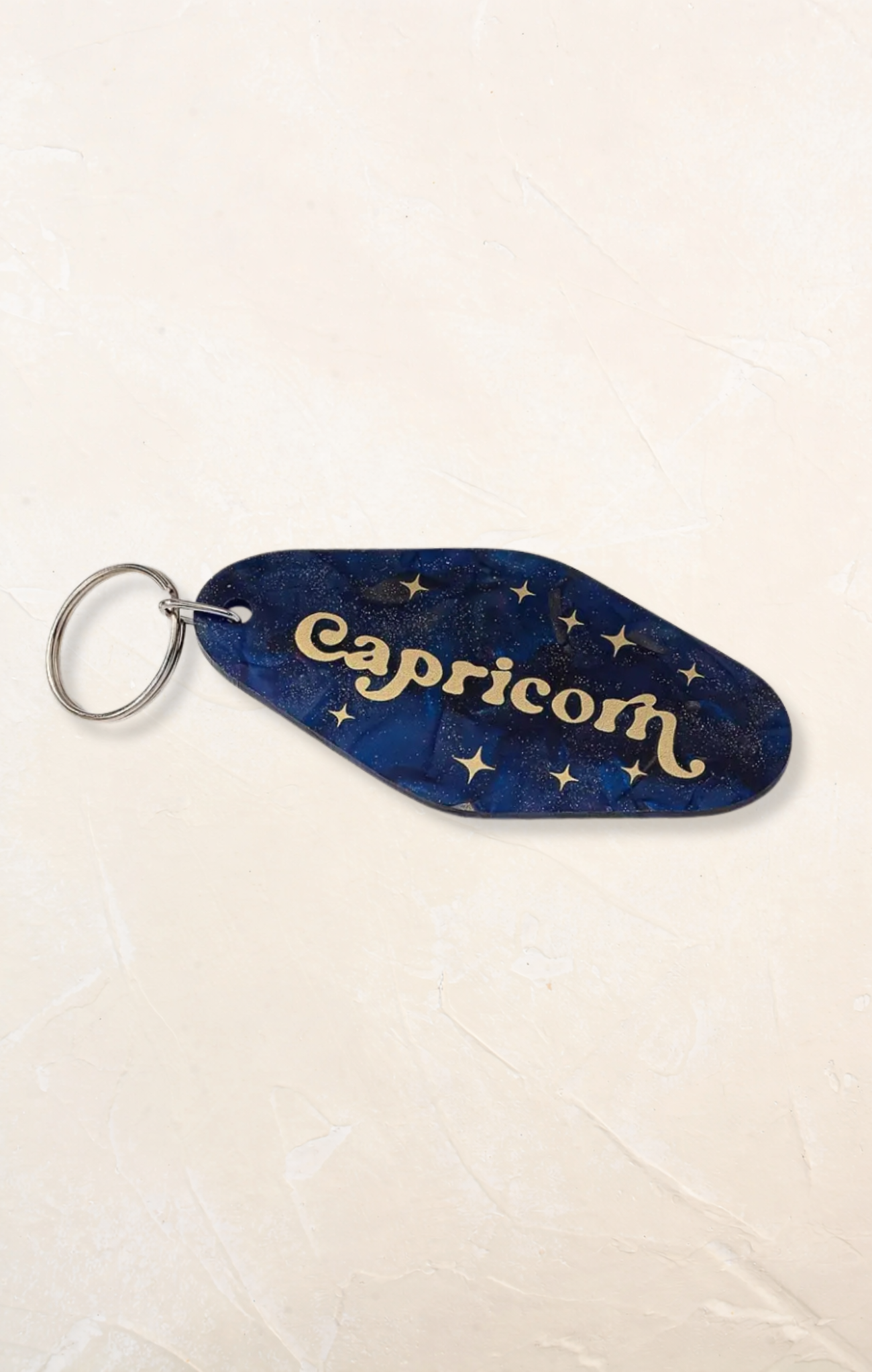 Keychain with 'Capricorn' text on a blue background with star patterns, on a light beige surface.