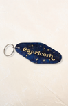 Keychain with 'Capricorn' text on a blue background with star patterns, on a light beige surface.