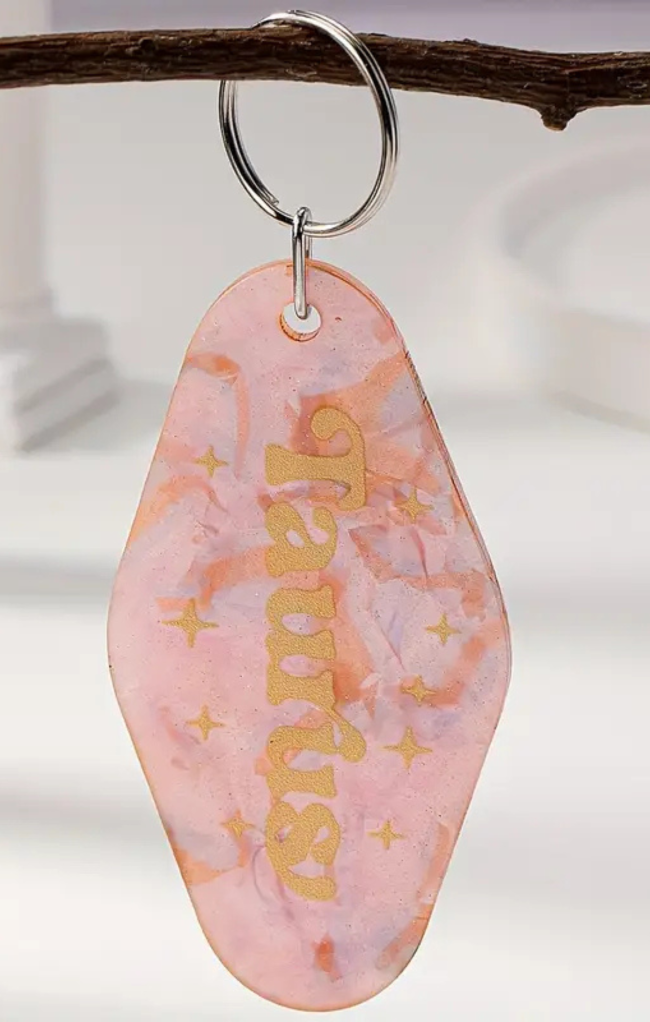 Pink keychain with gold text on a branch