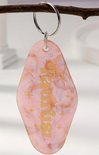 Pink keychain with gold text on a branch