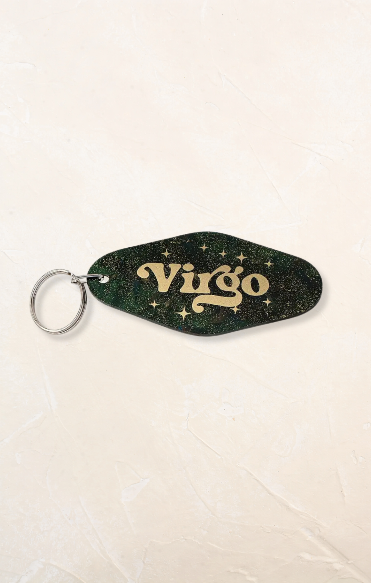 Keychain with 'Virgo' text on a green and gold design against a beige background