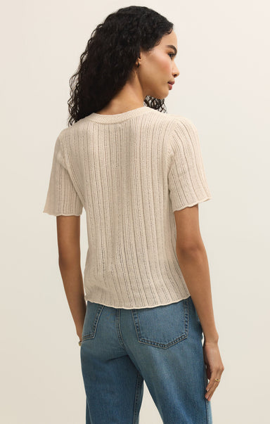 Woman wearing a beige ribbed sweater and blue jeans against a plain background