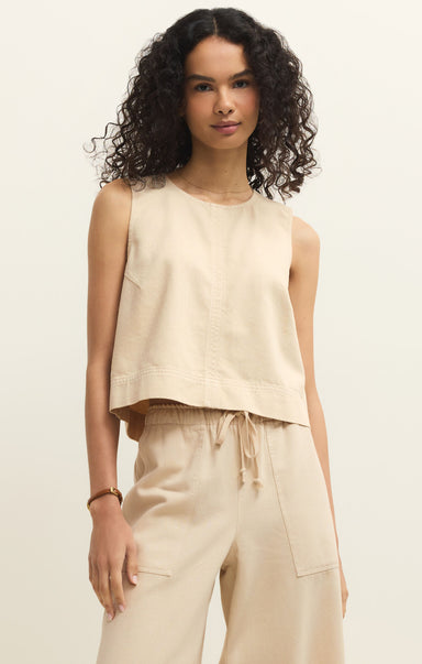 Woman wearing a beige sleeveless top and pants against a neutral background