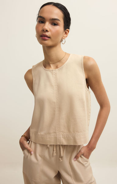 Woman wearing a beige sleeveless top and pants against a plain background