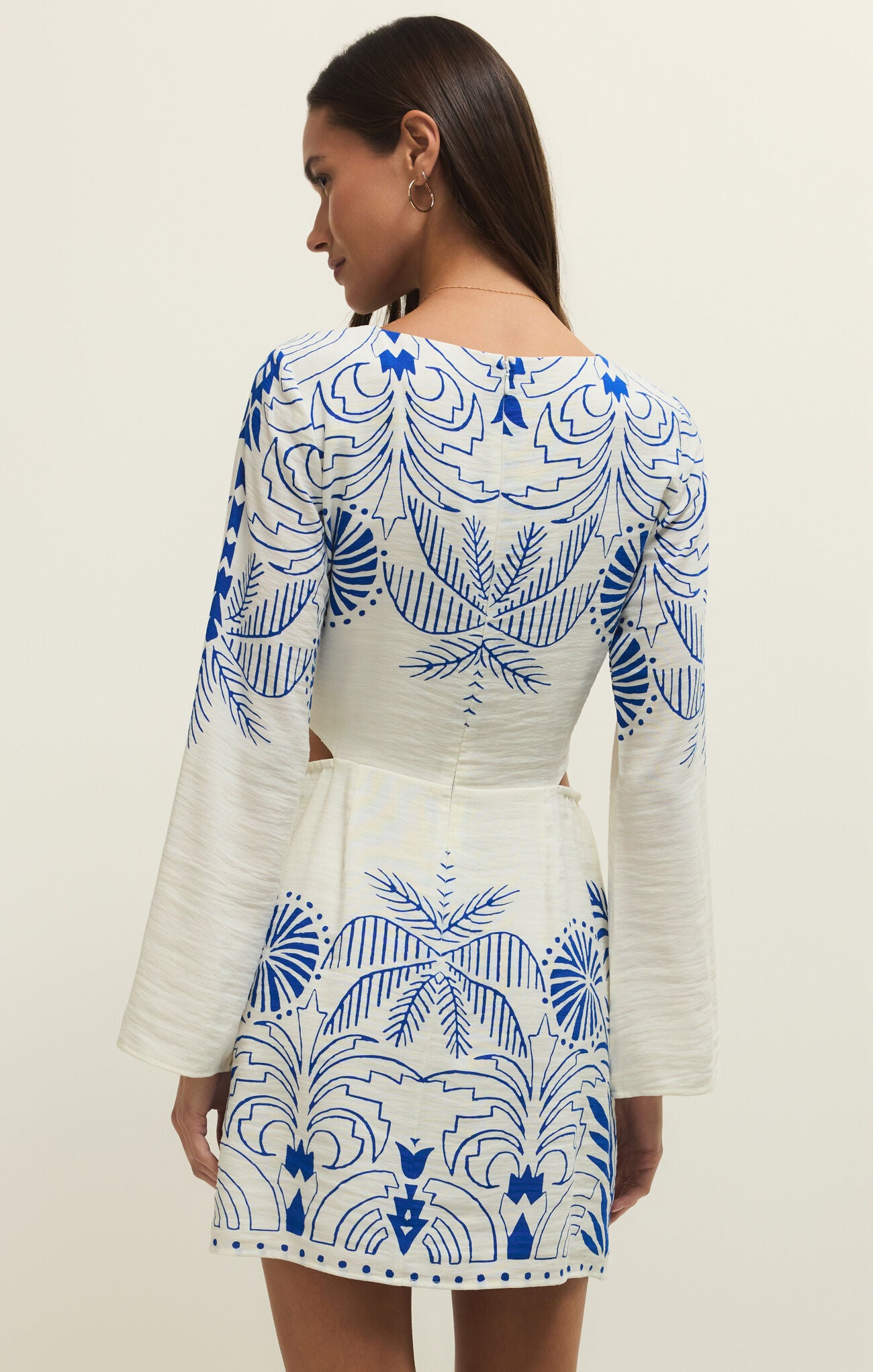 Woman wearing a white dress with blue patterns on a plain background