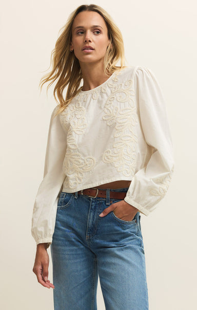 Woman wearing a white blouse with lace details and blue jeans on a plain background