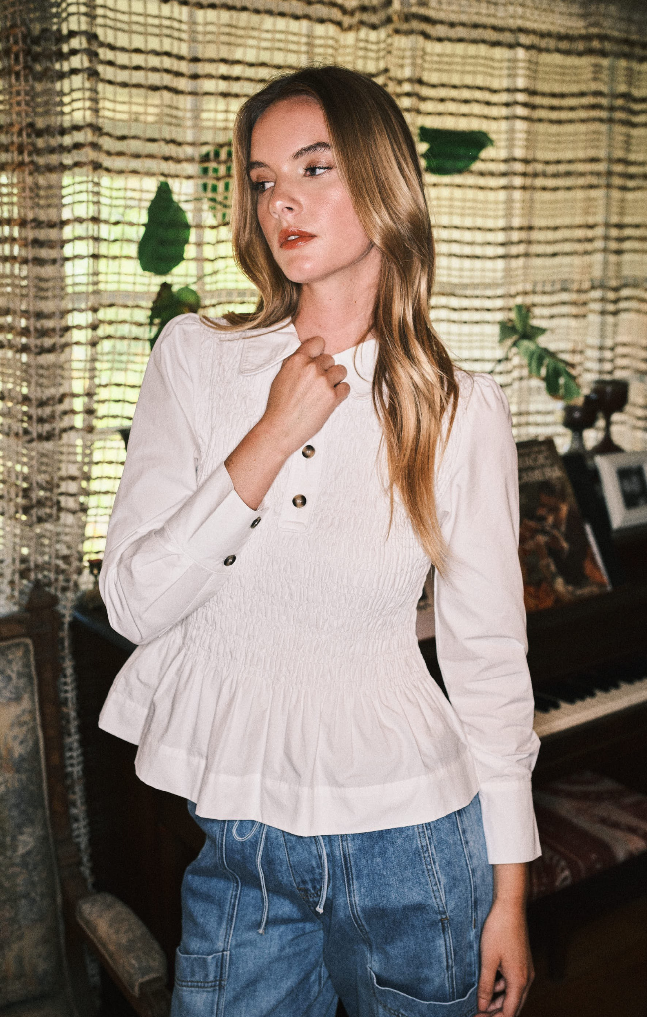 Woman wearing a white ribbed sweater and blue jeans in a room with decorative elements.