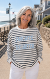 Woman wearing a striped sweater with 'Favorite Daughter' text on a beachside boardwalk.