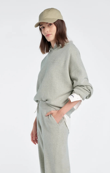 Person wearing a light gray sweatshirt and pants with a beige cap on a white background