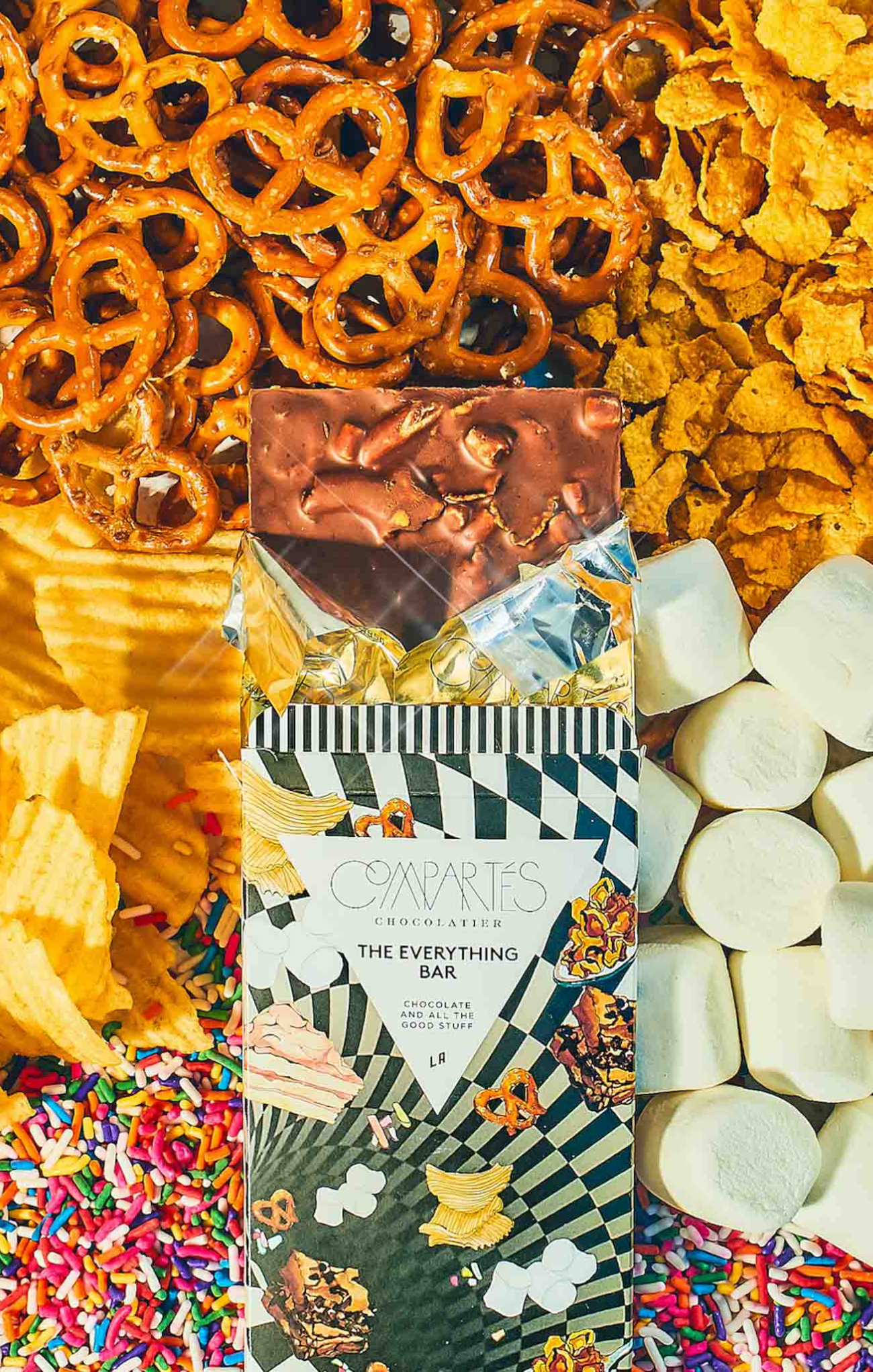 Candy bar packaging surrounded by snacks including pretzels, chips, and marshmallows.