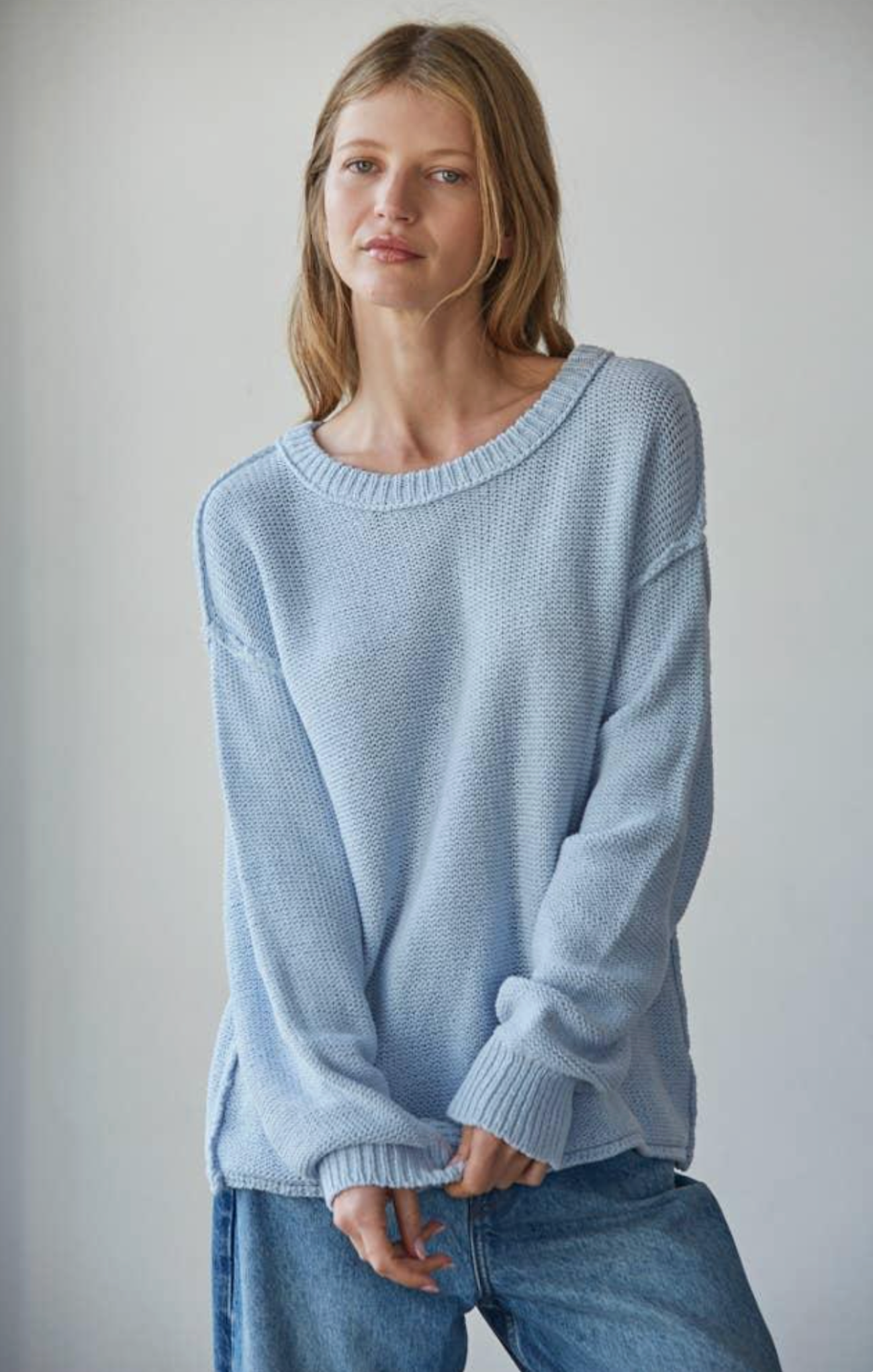 Woman wearing a light blue sweater and jeans against a plain background