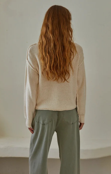 Person wearing a beige sweater and light green pants against a plain background