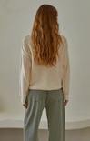 Person wearing a beige sweater and light green pants against a plain background