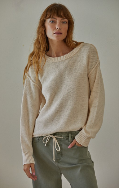 Woman wearing a beige sweater and green pants against a plain background
