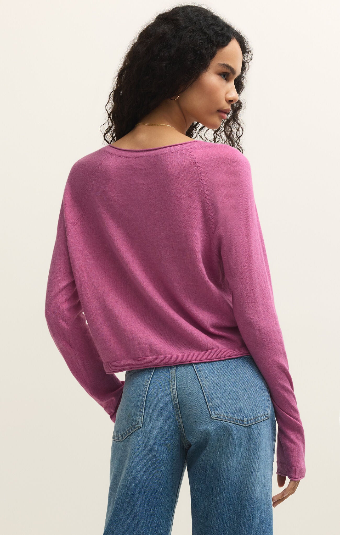 Woman wearing a pink sweater and blue jeans on a plain background