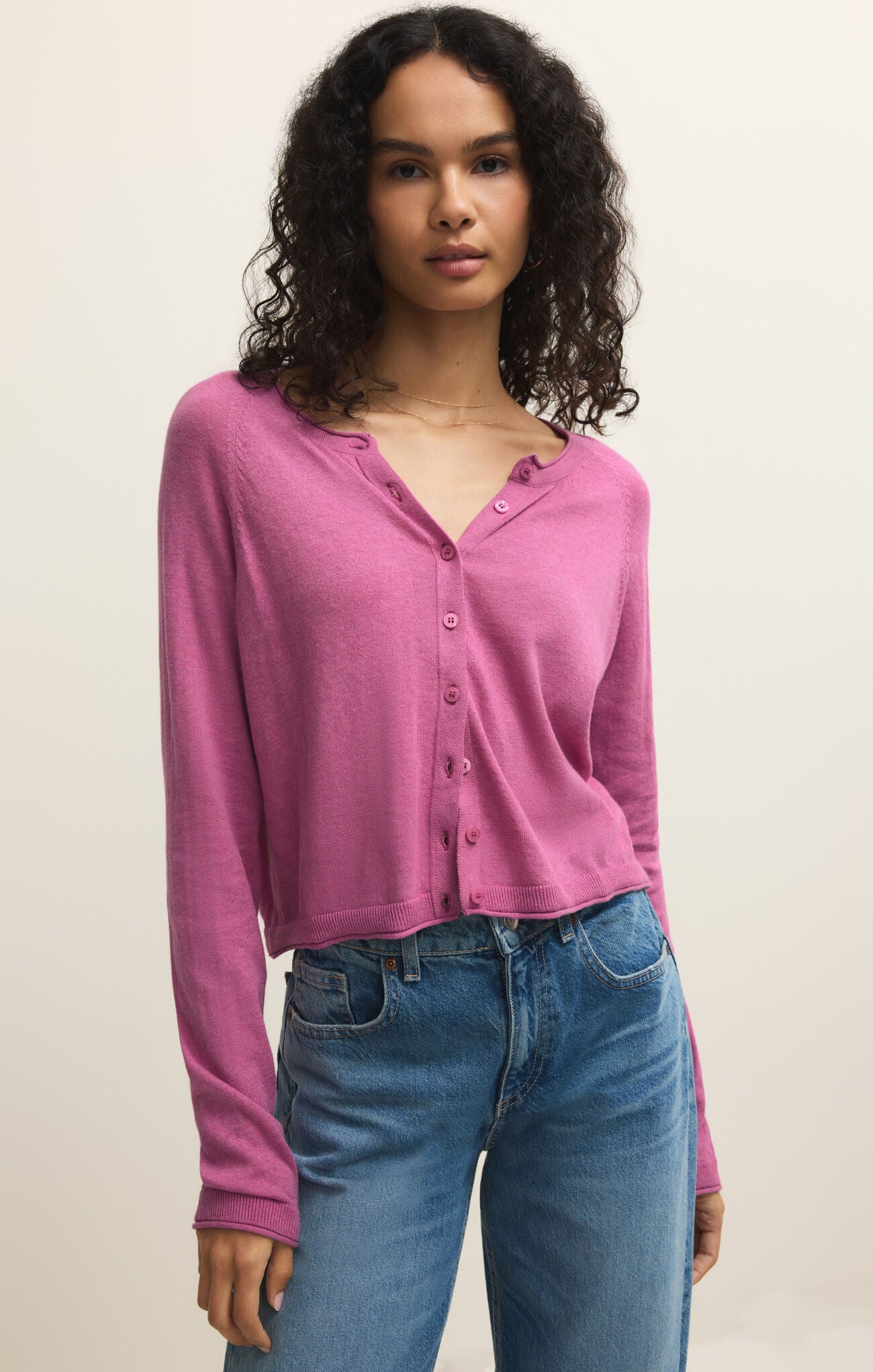 Woman wearing a pink long-sleeve shirt and blue jeans against a plain background