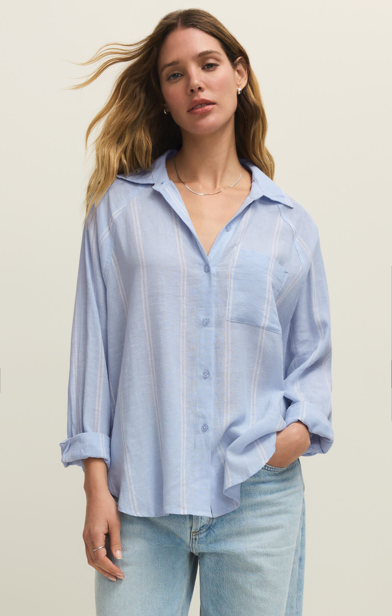 Woman wearing a light blue striped shirt and jeans against a plain background